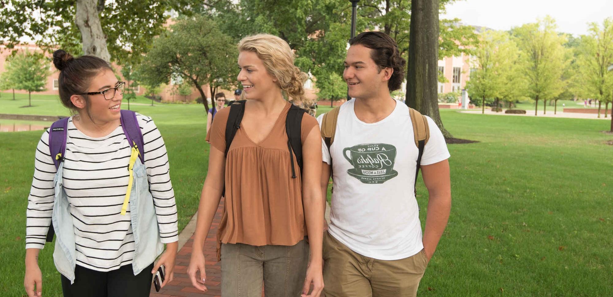 three students walking on sidewalk by campus lakes